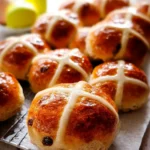 Fluffy hot cross buns with golden brown tops and pale crosses arranged on a serving tray