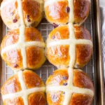 Traditional hot cross buns with glossy golden tops and pale crosses cooling on a wire rack