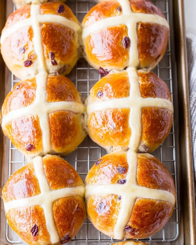 Traditional hot cross buns with glossy golden tops and pale crosses cooling on a wire rack
