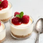 Easy Cheesecake Cups Recipe topped with raspberries and raspberry sauce in glass dessert cups