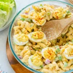 Macaroni Salad with Deviled Eggs in a glass bowl with creamy dressing and paprika topping