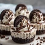 No-Bake Oreo Cheesecake Cups topped with whipped cream, Oreo cookies, and chocolate drizzle